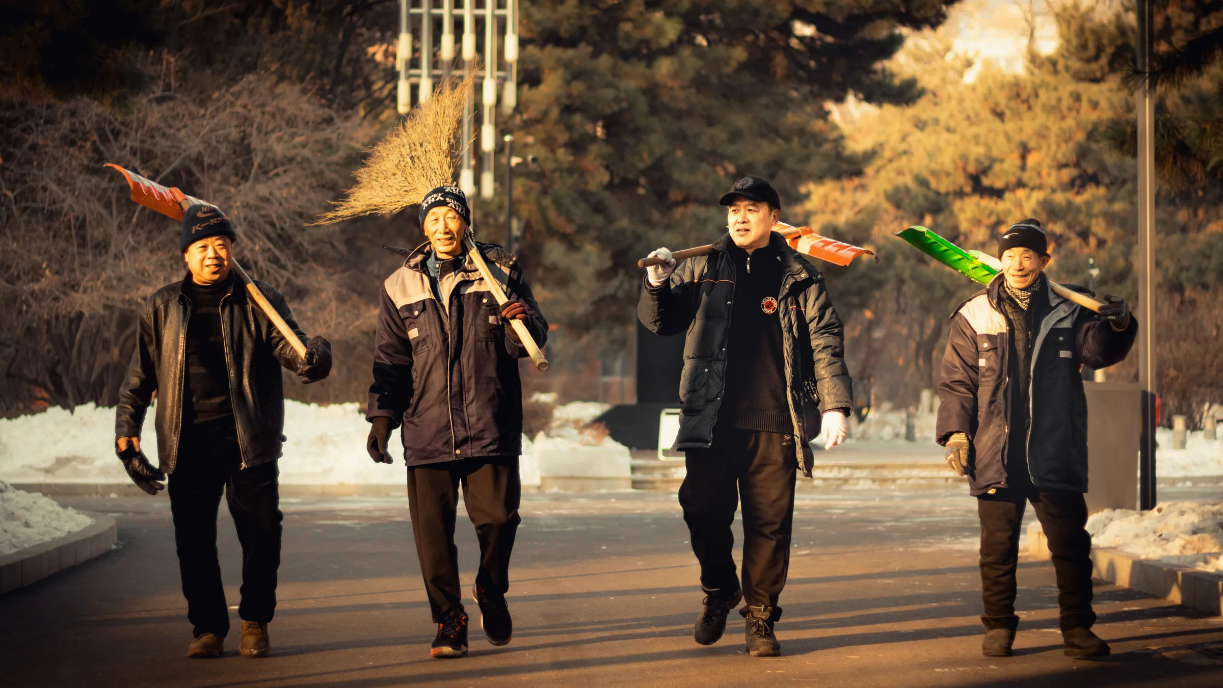 雪后晴朗的下午，四位工人扛着雪铲和扫把收工往回走，阳光映在他们脸上