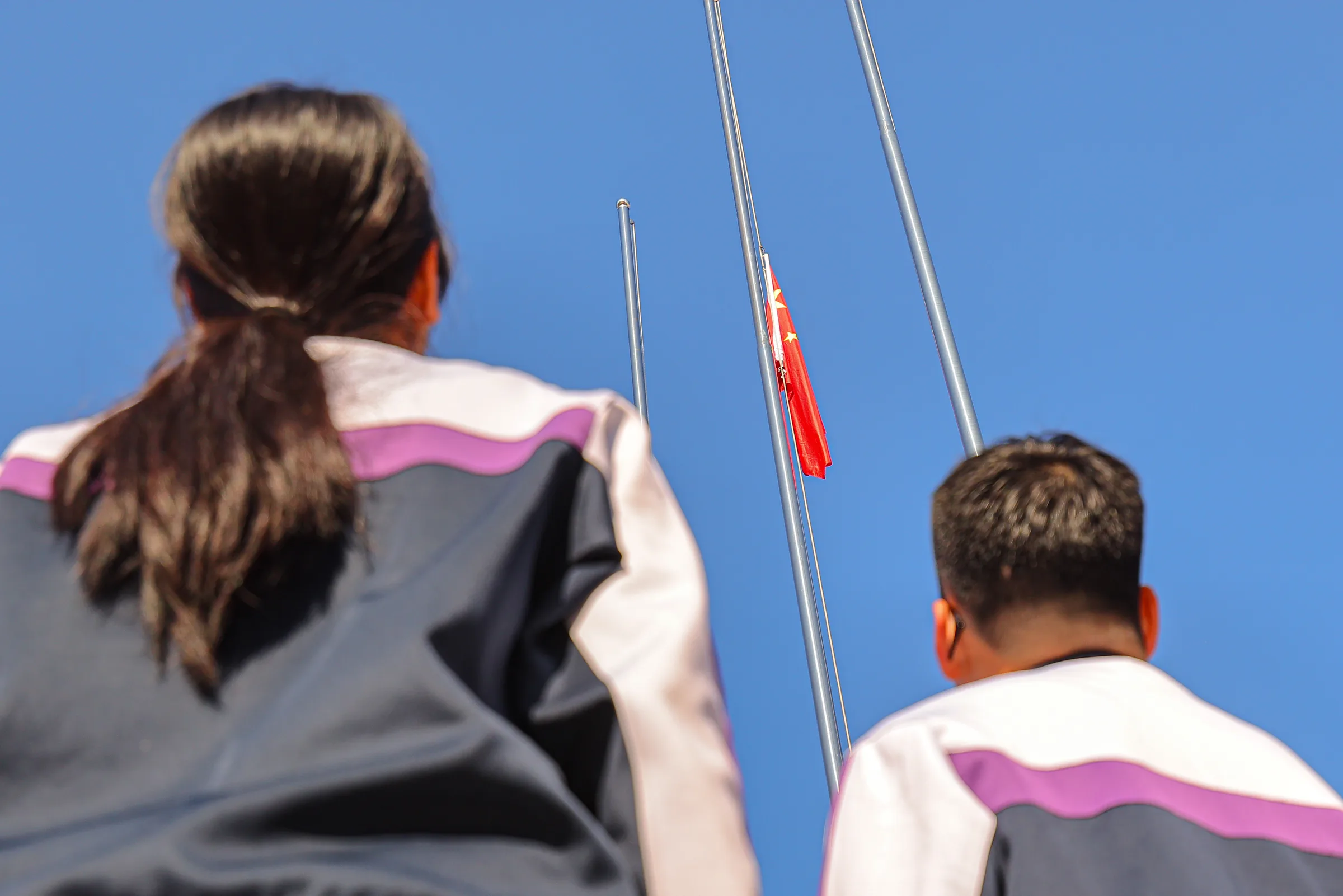 几位学生从背后望向升起的旗帜与蓝天