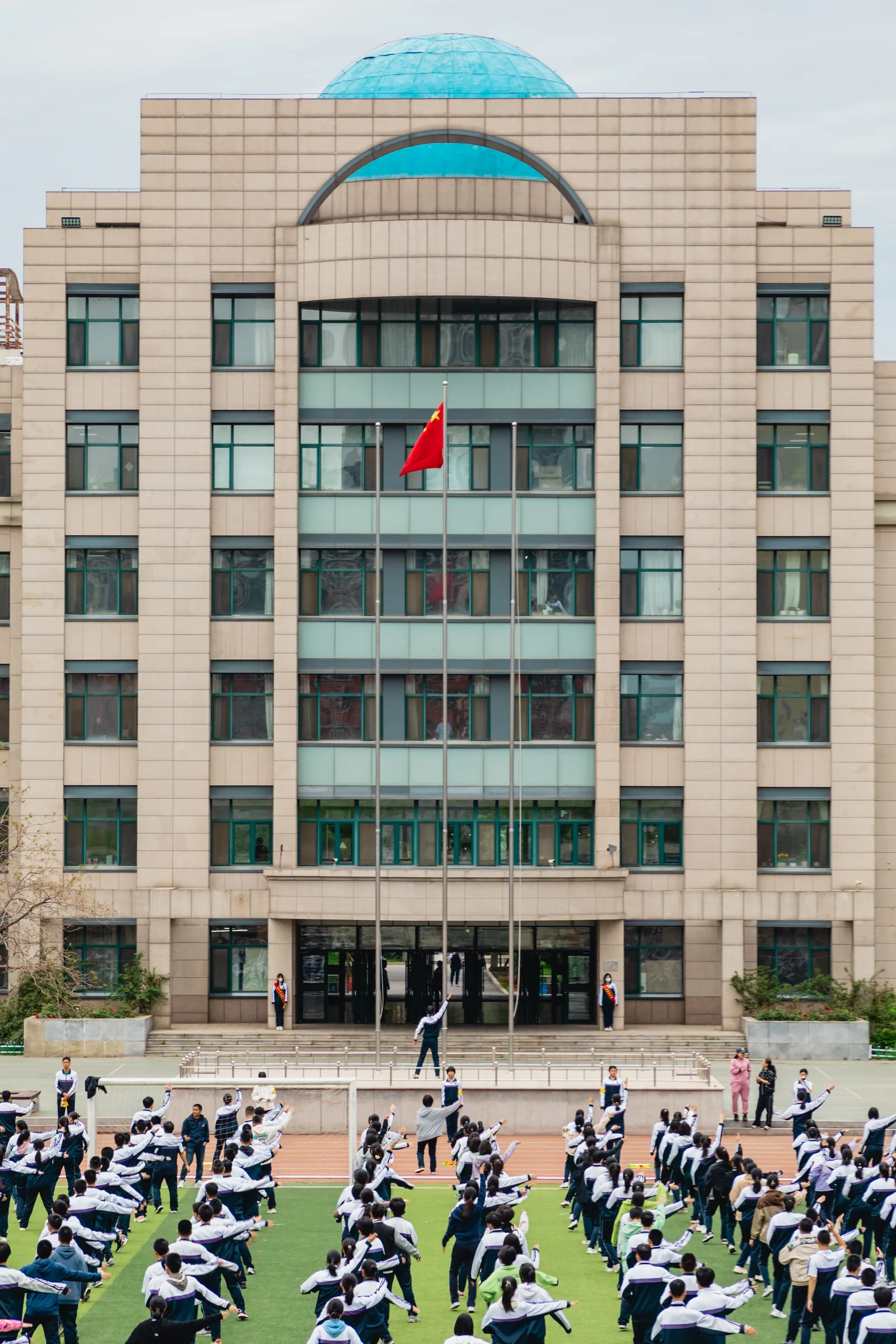 竖画幅收进主教学楼核心楼体、升旗台、国旗与做操的同学