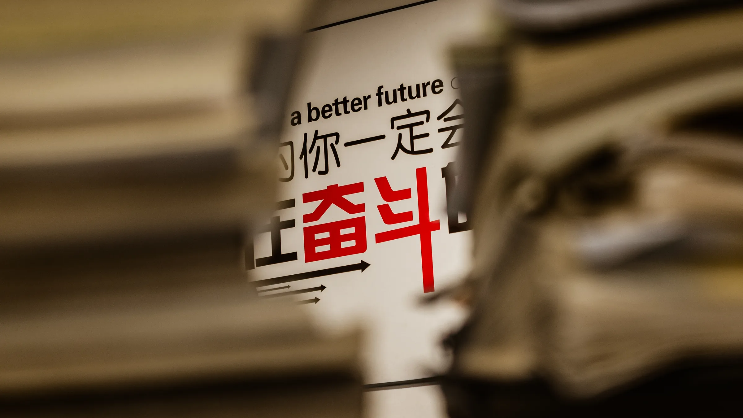 镜头从堆满课桌的书堆缝隙间拍向墙上标语里的“奋斗”二字